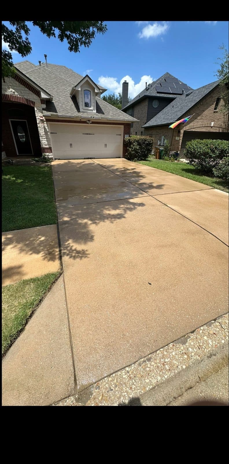 A freshly pressure-washed concrete driveway leading up to a two-story Austin, TX home under a blue sky